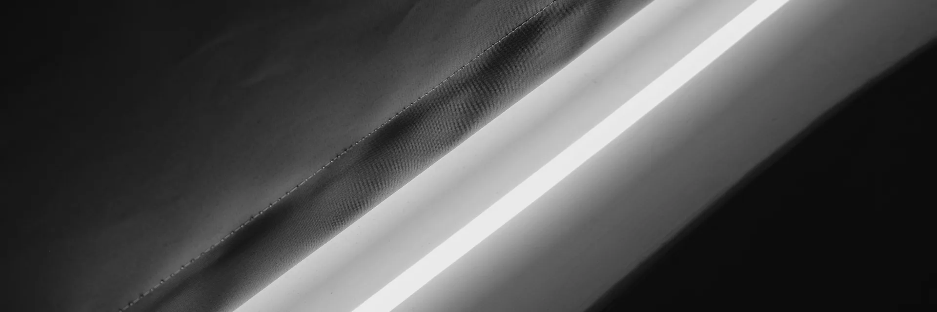 Zbliżenie na splot tkaniny rolety zaciemniającej z widocznym przeszyciem i pasem światła